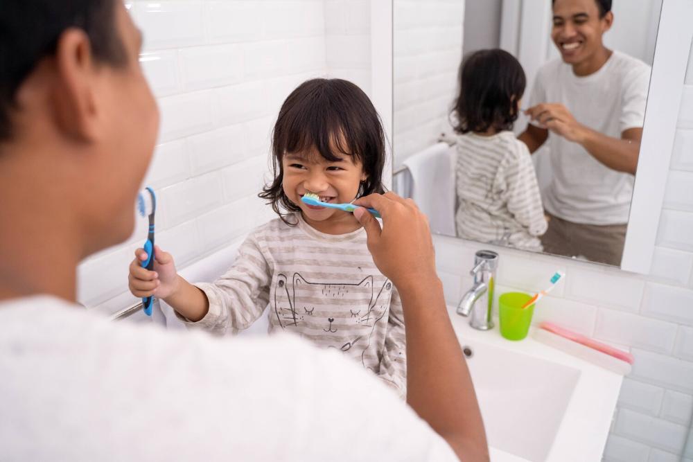 dad teaching young daughter how to brush her teeth