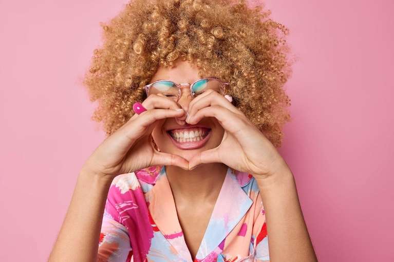 person smiling while holding heart hands